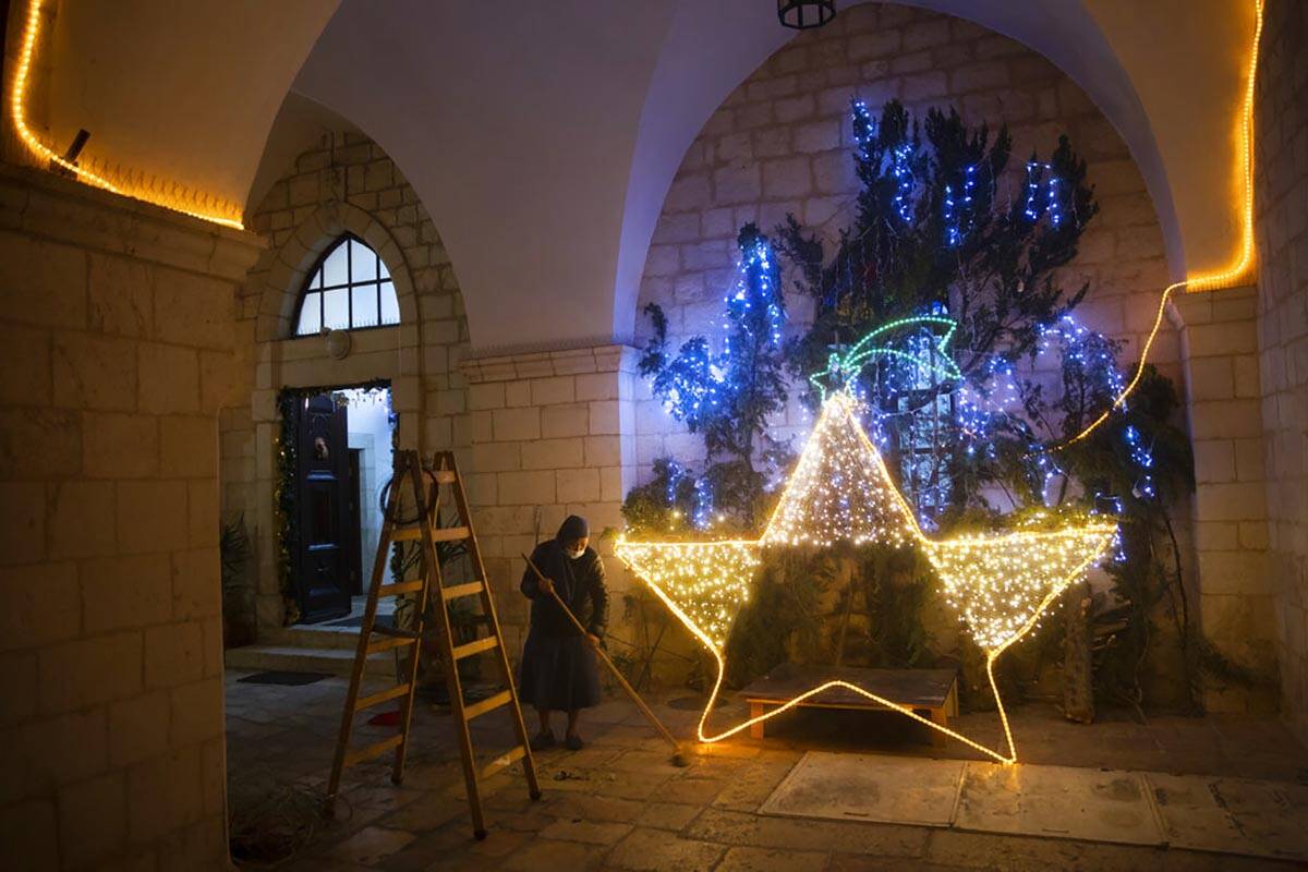 Una monja limpia el suelo tras decorar la entrada de una iglesia con luces navideñas, en la Ci ...